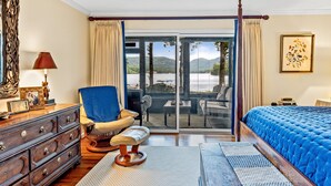 Une chambre avec un grand lit, une chaise, une commode et une vue sur un lac, visible à travers une porte-fenêtre coulissante.