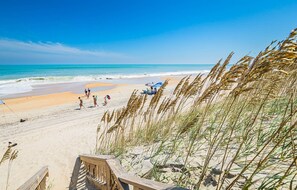 A beach with a wooden walkway leading to the shore, clear skies, and ocean waves. - Born To Sun - KDH MP 7.5, Oceanfront, Pool, Hot Tub, Pool Table, Foosball, Pets OK, Flex Stays (Kill Devil Hills)