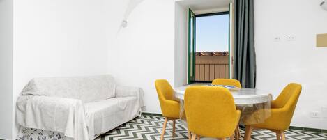 A modern room with a sofa, a dining table with yellow chairs, and a patterned floor.