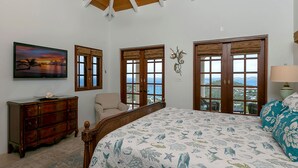 A bedroom with a large bed, a wooden dresser, a chair, and a painting on the wall. - Bananaquit Villa: Amazing Views! Large Pool! Full AC! (St John)