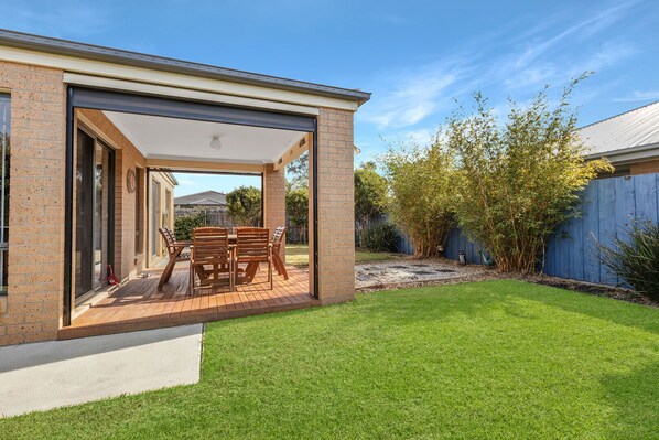 A covered patio with a table and chairs, a brick wall, and a grassy yard.