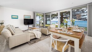 A modern living room with a large dining table set for a meal, a sofa, and a TV. - Tranquil Waters - Luxury Waterfront Home  with Stunning Views (Salamander Bay)