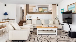 A modern living room with a sofa, coffee table, and TV. There is a staircase leading to an upper level. - Tranquil Waters - Luxury Waterfront Home  with Stunning Views (Salamander Bay)