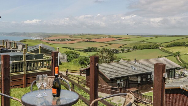 A table with a bottle and glasses, overlooking a scenic landscape with fields and a distant body of water. - Three Views Lodge (Torpoint)