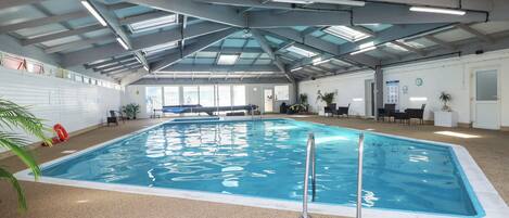 An indoor swimming pool with a ceiling structure, a lifebuoy, and a wall with a fire exit sign.
