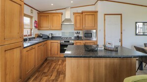 A kitchen with wooden cabinets, a central island, a microwave, and a gas stove. - Three Views Lodge (Torpoint)