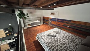 A modern bedroom with a wooden floor, a patterned bedspread, a bedside table, and a hanging light fixture.