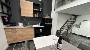 A modern kitchen with a dining area, featuring a white table with a bottle of wine and glasses, a microwave, and a sink.
