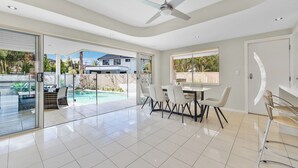 Un vaste espace de vie avec une porte vitrée donnant sur une piscine, un ventilateur de plafond et une table à manger avec des chaises.