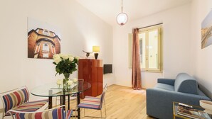 Ein modernes Wohnzimmer mit einem Glastisch, gestreiften Stühlen, einem blauen Sofa und einem großen Fenster mit Vorhängen.