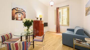 Una sala de estar moderna con una mesa de comedor de vidrio, sillas a rayas, un sofá azul y un gran ventanal con cortinas.