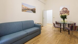 Ein Wohnzimmer mit einer Couch, einem Esstisch mit Stühlen und zwei an der Wand hängenden Bildern.
