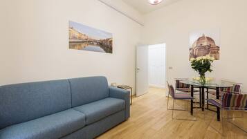 Una sala de estar con un sofá, una mesa de comedor con sillas y dos cuadros colgados en la pared.