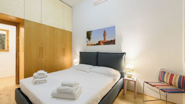 Ein Schlafzimmer mit einem Bett, einem Nachttisch mit Lampe, einem Sessel und einem Kleiderschrank.