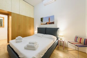 A bedroom with a bed, a nightstand with a lamp, a chair, and a wardrobe.
