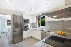 A modern kitchen with stainless steel appliances, granite countertops, and a window providing natural light. - Villa Estanyol (Campos)