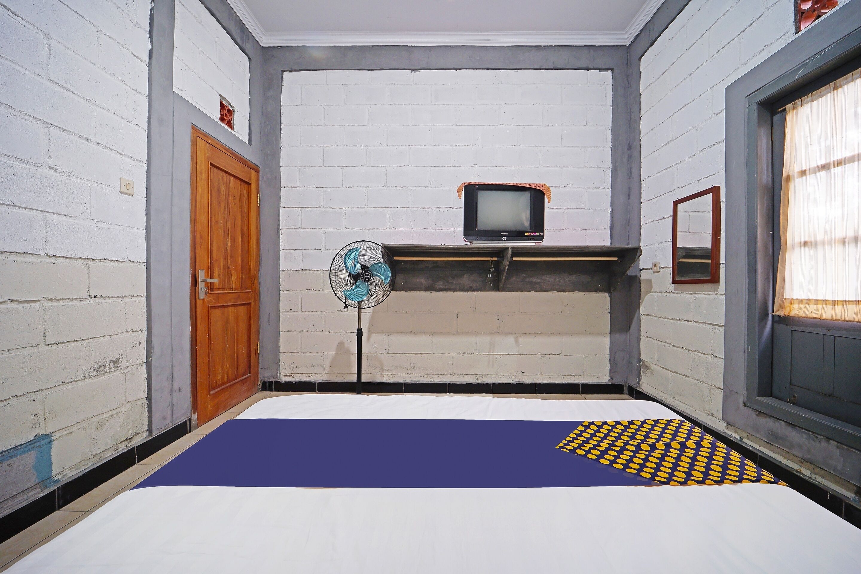 A small, narrow room with a bed, a television, and a fan.