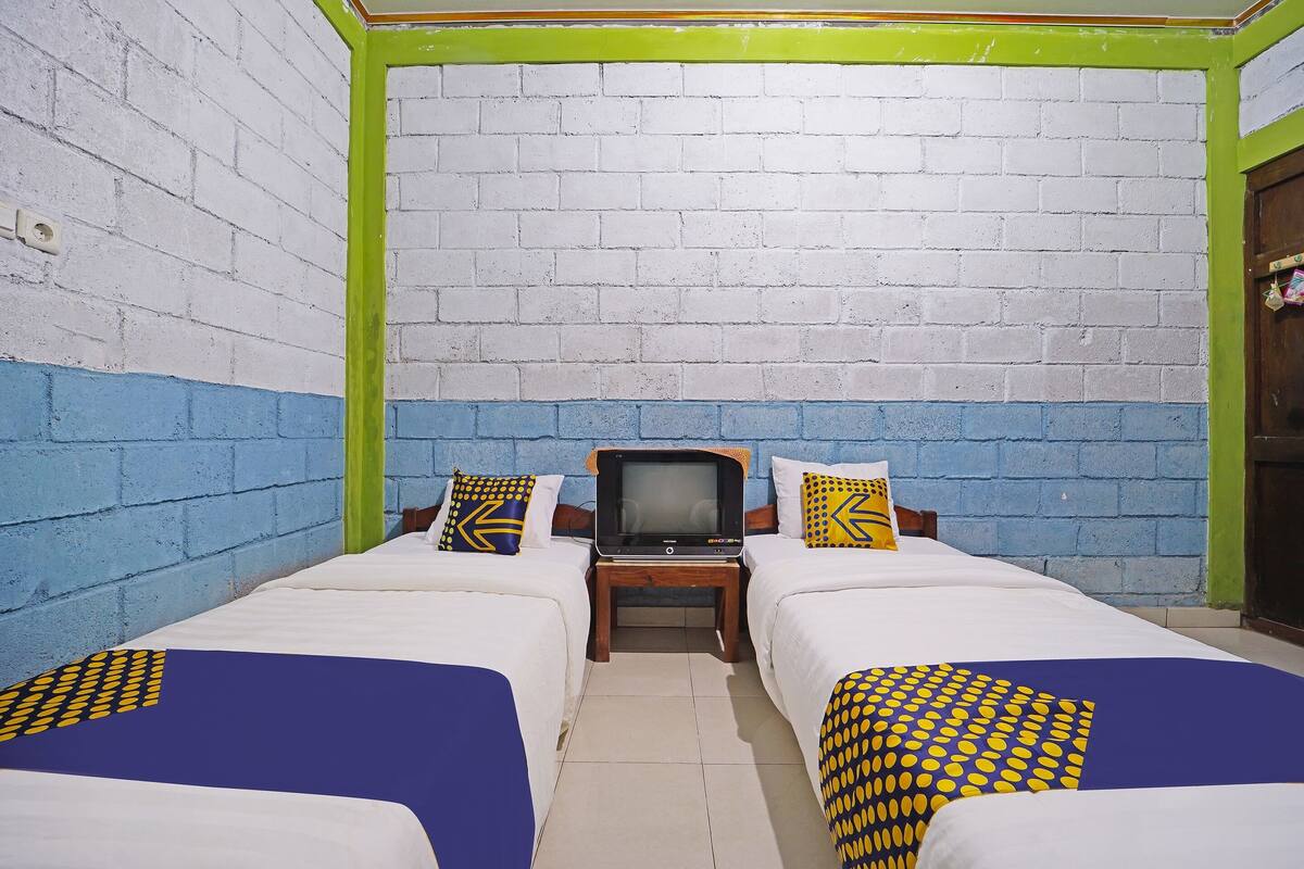 Une chambre avec deux lits, une télévision et un mur en briques.