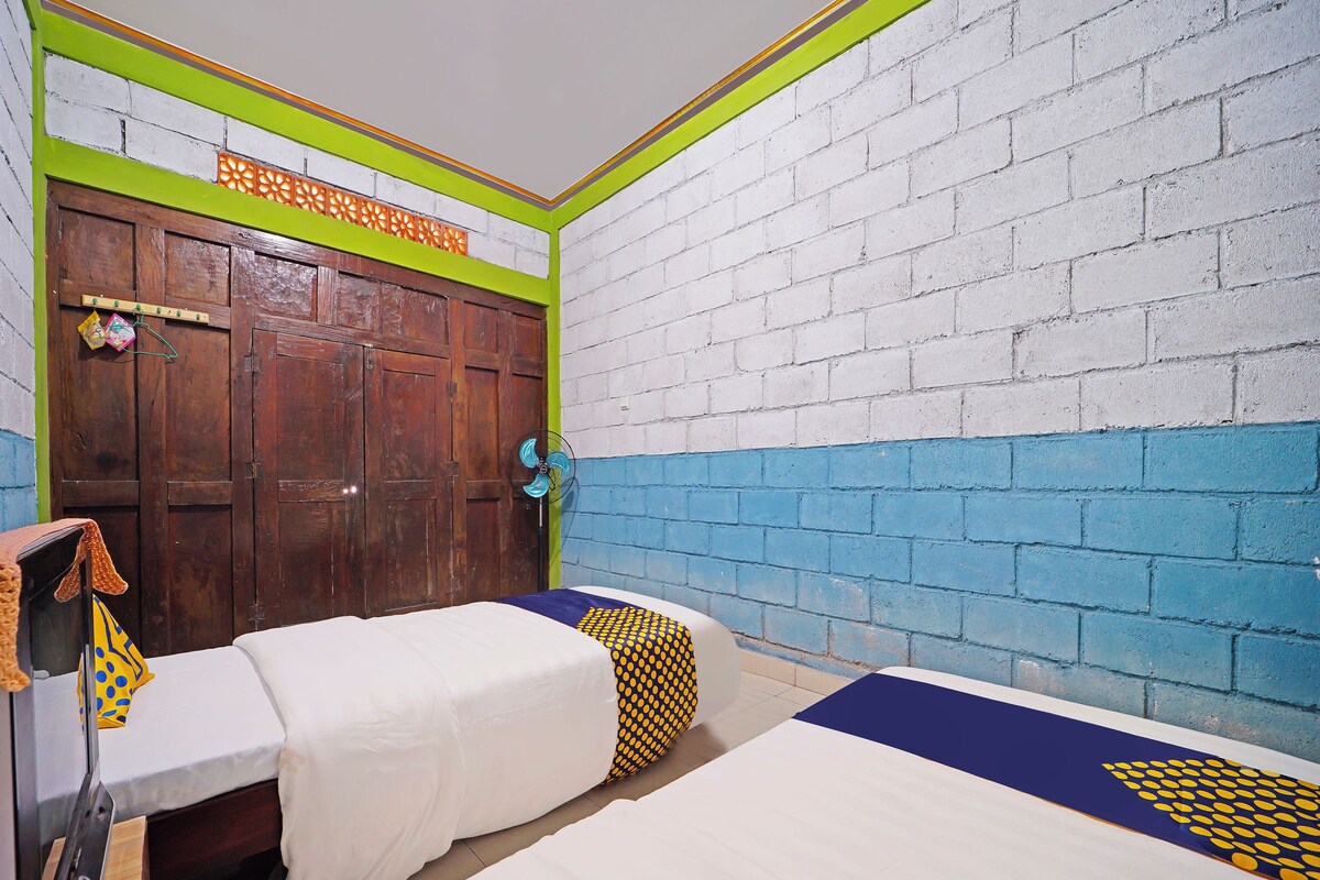 Une chambre avec deux lits, une armoire en bois et un mur dont le motif est constitué de briques.