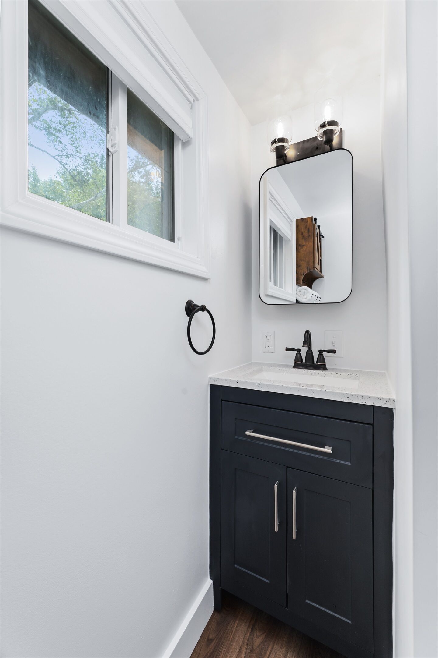 Une salle de bain avec un meuble-lavabo blanc, des armoires sombres, un miroir avec éclairage intégré et une fenêtre.