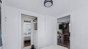 A bedroom with a bed, a walk-in closet, and a TV in the adjacent room.