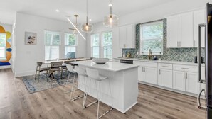 Una cocina moderna con armarios blancos, una isla grande con taburetes de bar, iluminación colgante y un salpicadero de baldosas tipo espiga.