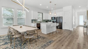 Una cocina moderna con armarios blancos, una isla central y un área de comedor con una mesa larga y sillas.