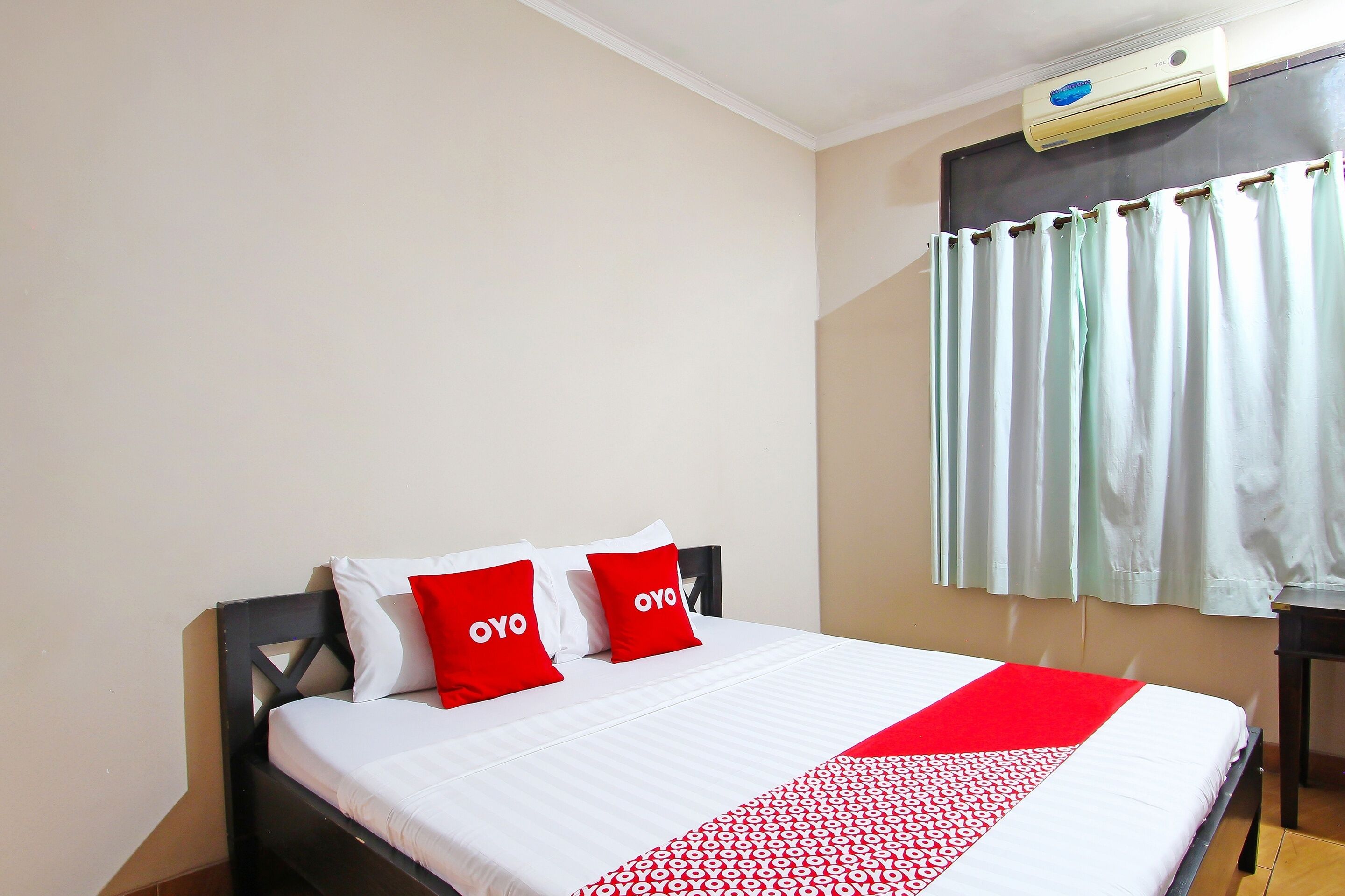A neatly made bed with white and red bedding, a black headboard, and a red and white patterned throw.