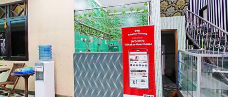 Zona de recepción de un hotel con dispensador de agua, un cartel y una escalera.