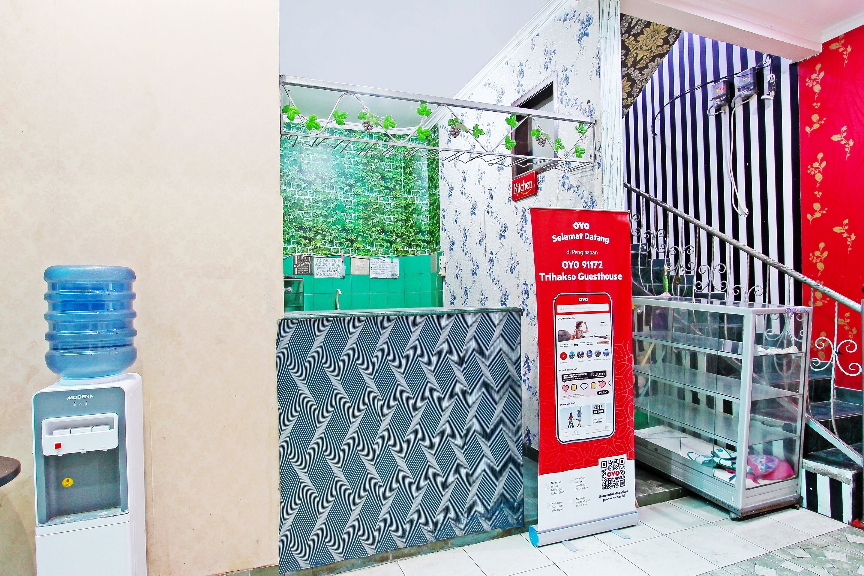 A reception area with a water dispenser, a signboard for OYO Trihaksos Guesthouse, and a staircase with a railing.