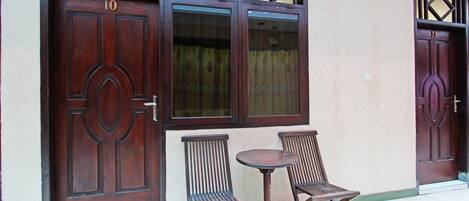A building with two large wooden doors, a window with a curtain, and two wooden chairs and a small table outside.