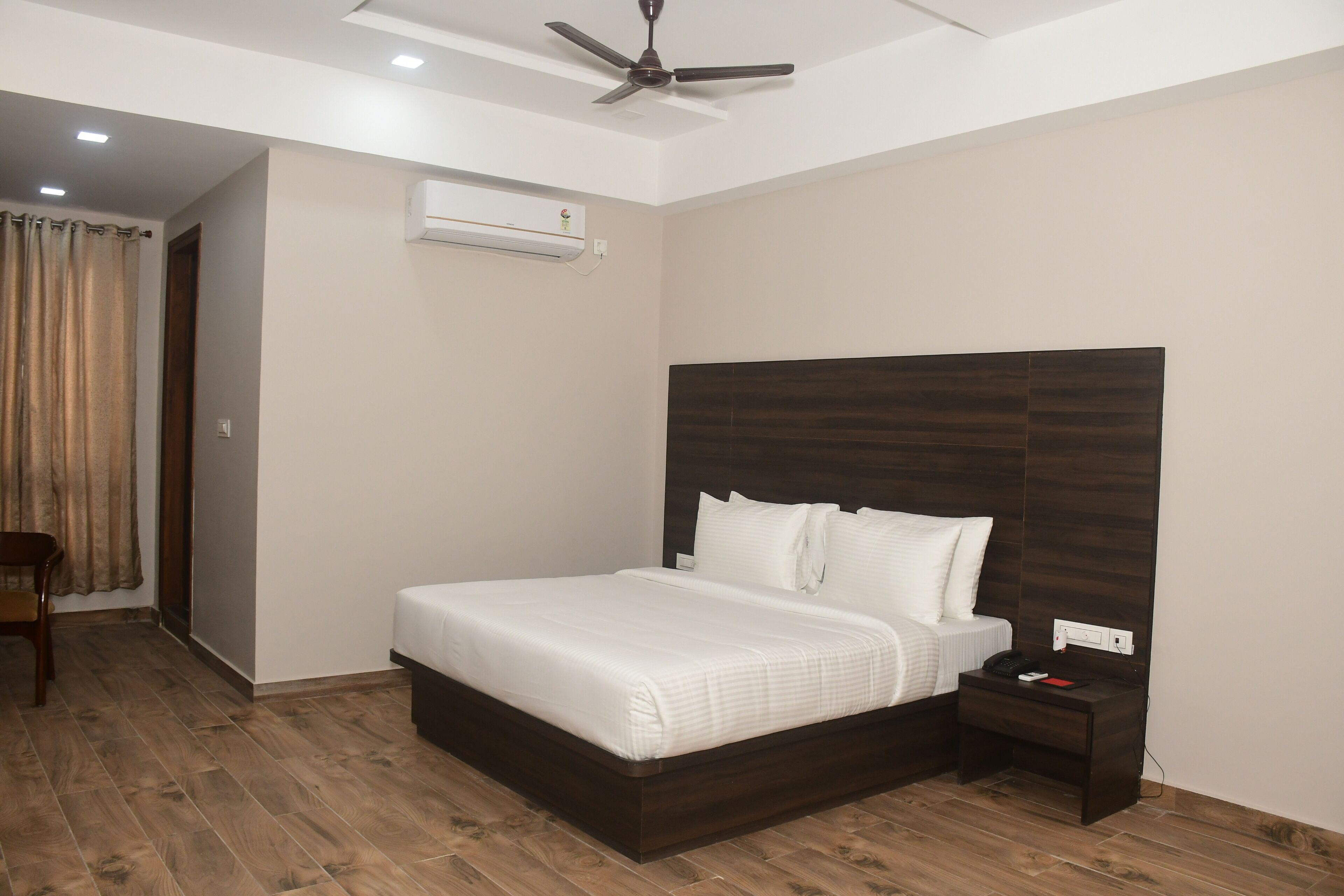 A bedroom with a bed, a nightstand, a ceiling fan, and an air conditioning unit.