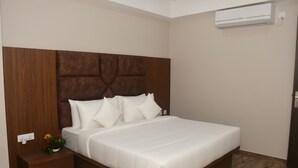 Une chambre avec une tête de lit en bois, un couvre-lit blanc, une table de chevet avec une plante et un appareil de climatisation fixé au mur.