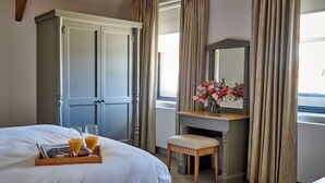 Een hotelkamer met een bed, een houten bureau, een stoel, een dressoir en een raam met gordijnen.