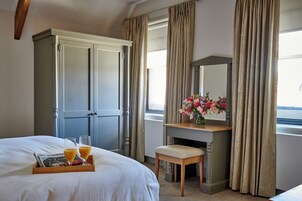 A hotel room with a bed, a wooden desk, a chair, a dresser, and a window with curtains.