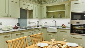 Een keuken met lichtgroene kastjes, een granieten aanrechtblad, een Bosch oven en een eettafel gedekt met wijnglazen en kaas.