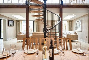 Un comedor con una mesa de madera dispuesta para seis personas, una escalera de caracol y vista al salón.