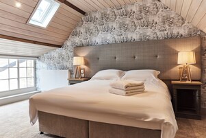 Un dormitorio con una cama grande, dos mesitas de noche con lámparas, un tragaluz y una pared con estampado.