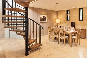 Un interior moderno con una escalera en espiral, una mesa de comedor de madera, sillas y un cuadro en la pared.