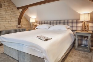 A bedroom with a large bed, two bedside lamps, a brick wall, and a sloped ceiling.