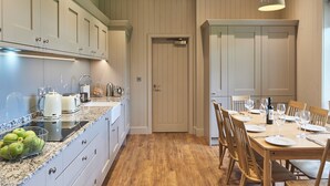 Une cuisine avec des meubles blancs, un plan de travail en granit et un coin repas avec une table en bois, mise pour six personnes.