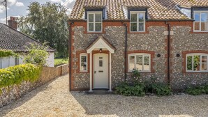 Uma casa de dois andares com telhado de telhas, fachada de tijolos e entrada por um caminho de brita.