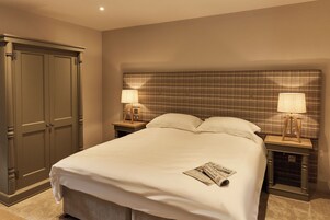 Habitación de hotel con una cama grande, dos mesitas de noche con lámparas, un armario y un cabecero estampado.
