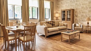 A dining area with a wooden table set for four, surrounded by chairs. A sofa and a cabinet are also visible in the room. - The Stalls (Hexham)