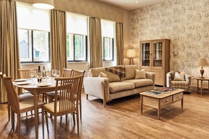 Un comedor con una mesa de madera dispuesta para cuatro personas, rodeada de sillas. También se puede ver un sofá y un aparador en la habitación.
