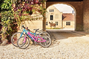 A bicycle parked under a stone archway with a building and a donkey statue in the background.