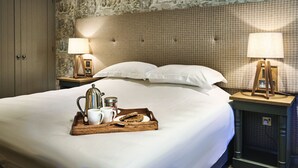Cama bem arrumada com uma bandeja de itens de café da manhã, duas luminárias de cabeceira e papel de parede estampado.