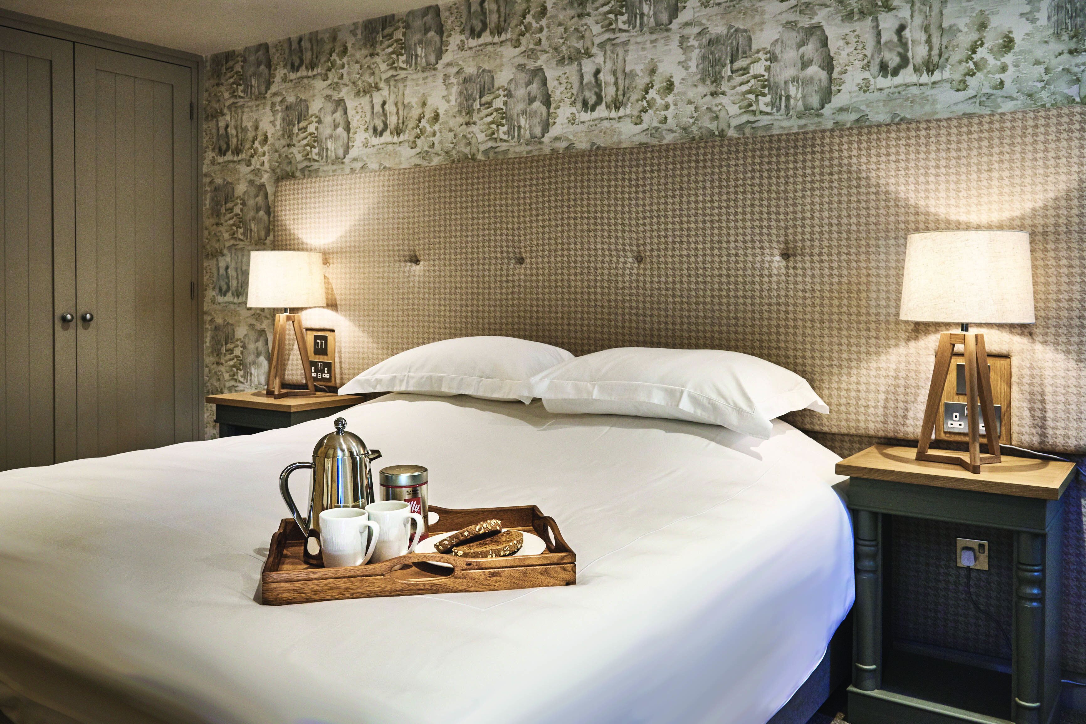 A neatly made bed with a tray of breakfast items, two bedside lamps, and a patterned wallpaper.