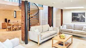 A spacious living area with a modern staircase, two sofas, a coffee table with fruit, and a dining set. - The Carriage House (Hexham)