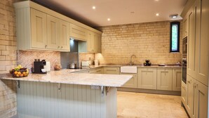 A kitchen with light-colored cabinets, a marble countertop, and a brick wall. - The Carriage House (Hexham)